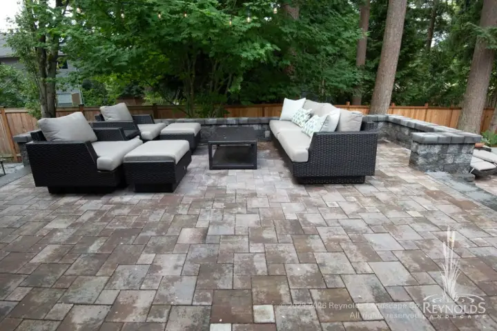 Spacious paver patio with cushioned sectional sofa and lounge seating surrounded by mature trees