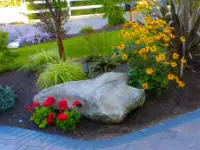 Large boulder anchors a garden corner.