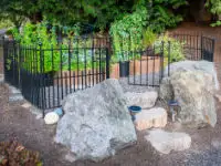 Boulders sete the entrance to a metal fenced vegetible garden.