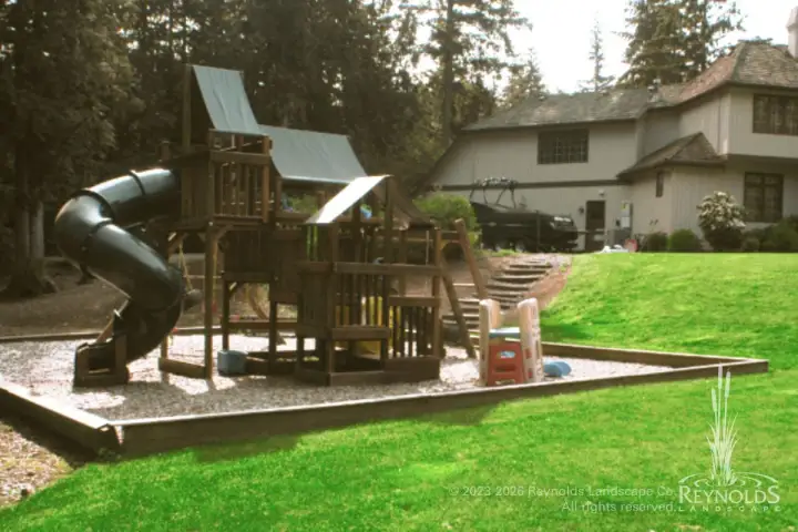 Large backyard play structure with tube slide on gravel safety surface and lawn