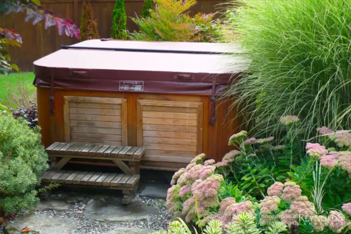 Hot tub nestled in lush PNW garden with ornamental grasses and sedum
