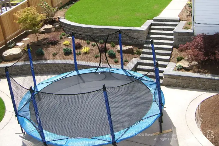 Backyard trampoline with paver retaining wall stairway and terraced garden