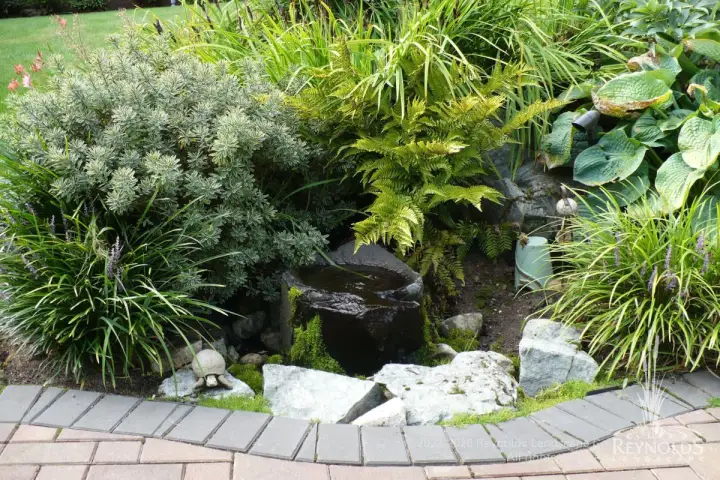 Small pond with boulder surround and river rock edging nestled among Japanese forest grass, dwarf conifers, and mixed evergreen shrubs in a Pacific Northwest garden