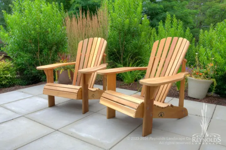 Two cedar Adirondack chairs on a paver patio surrounded by ornamental grasses and mixed evergreen shrubs in a Pacific Northwest garden
