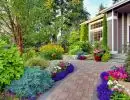 Colorful front yard garden with paver walkway, container plantings of petunias and annuals, and mixed perennial beds with purple salvia and marigolds alongside a craftsman home