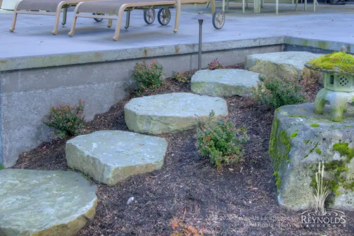Large natural stepping stone path with irregular granite slabs set in bark mulch planting bed with ornamental shrubs