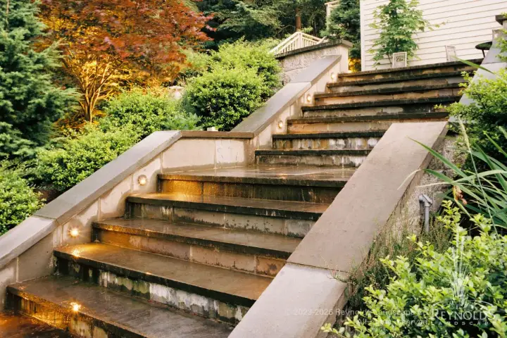 Broad bluestone tread stair steps with stone cap walls and low-voltage lighting surrounded by lush fall foliage