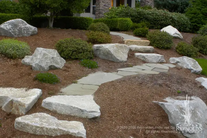 White granite stepping stone path winding through a dry gravel garden with natural boulders and shrubs
