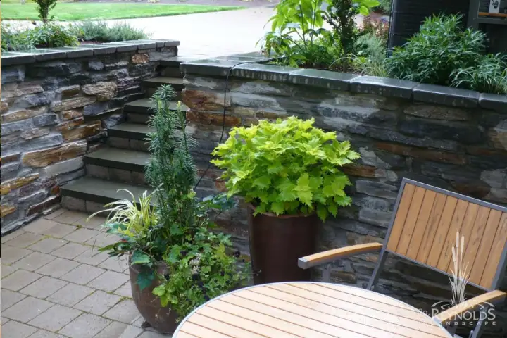 Dry stack natural stone wall with container plantings and wood patio furniture on paver patio