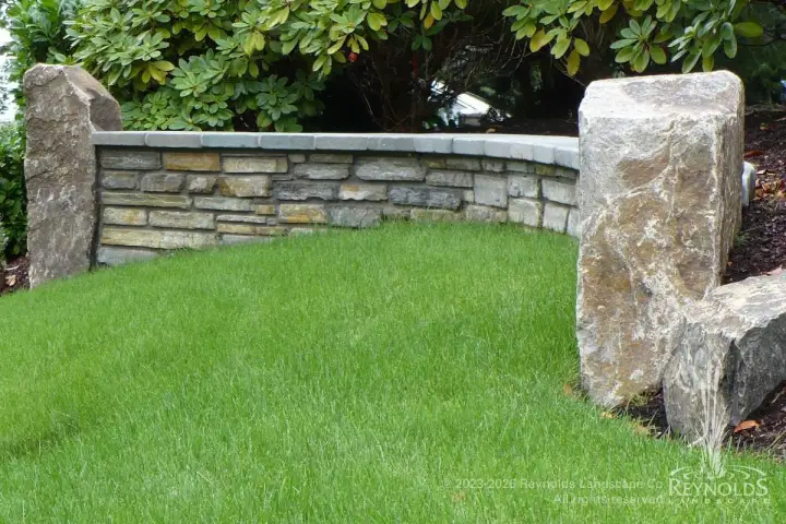 Natural stone garden wall with large boulder end caps and manicured lawn in open backyard setting