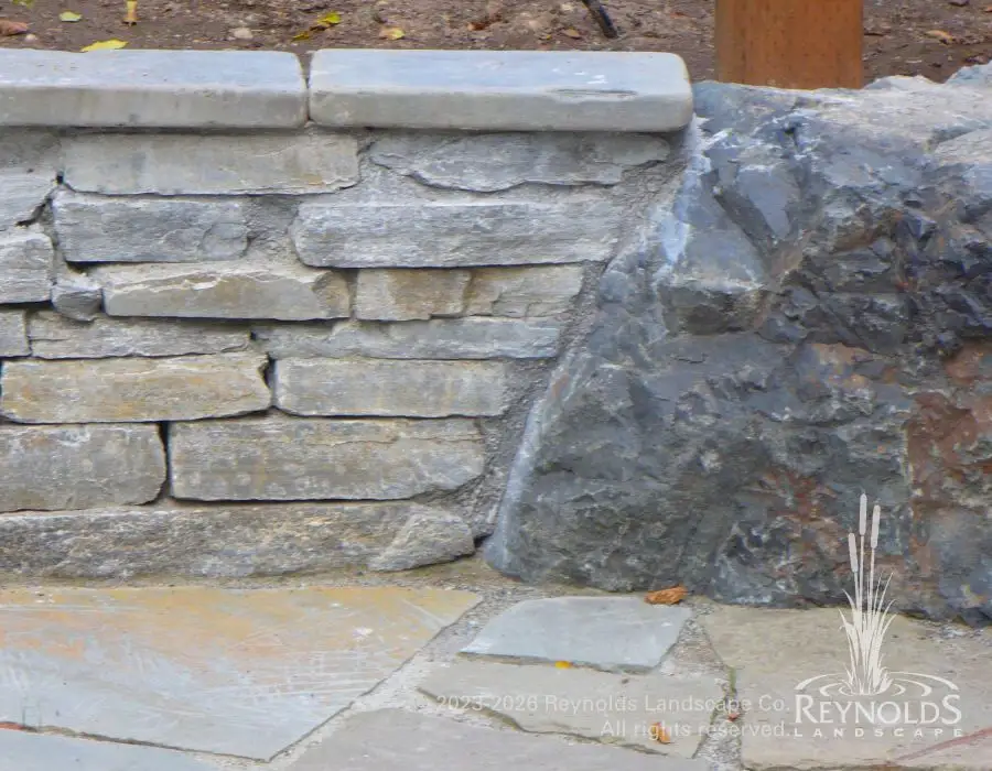 Large basalt boulder accent at corner of dry stack natural stone retaining wall on flagstone patio