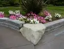 Corner concrete block raised planting bed with natural stone corner accent and colorful annual flowers along driveway